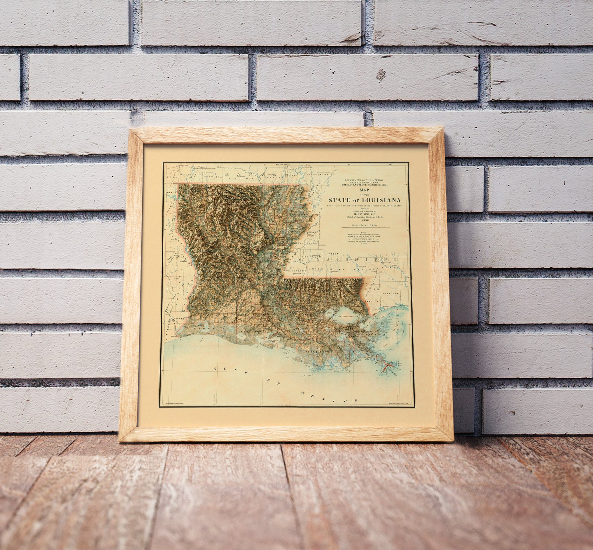 Vintage Louisiana shaded relief map in a wooden frame. Realistic terrain art print for home decor, displayed against a brick wall
