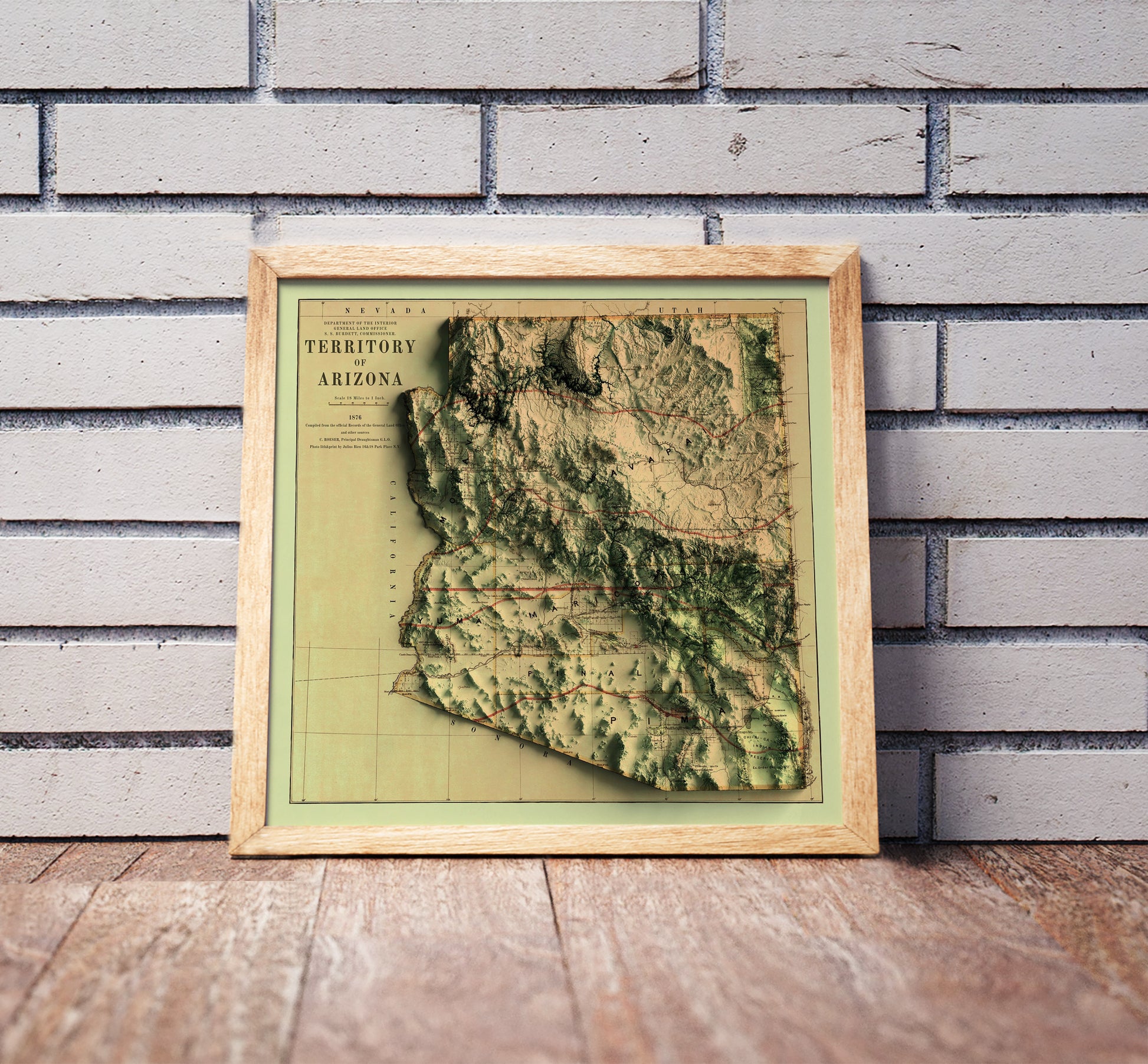 Vintage Arizona shaded relief map in a wooden frame. Realistic terrain art print for home decor, displayed against a brick wall