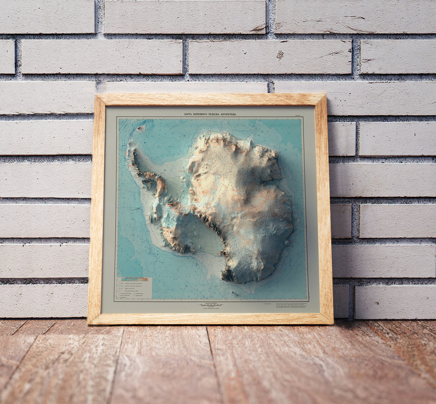 Vintage Antarctica shaded relief map in a wooden frame. Realistic terrain art print for home decor, displayed against a brick wall