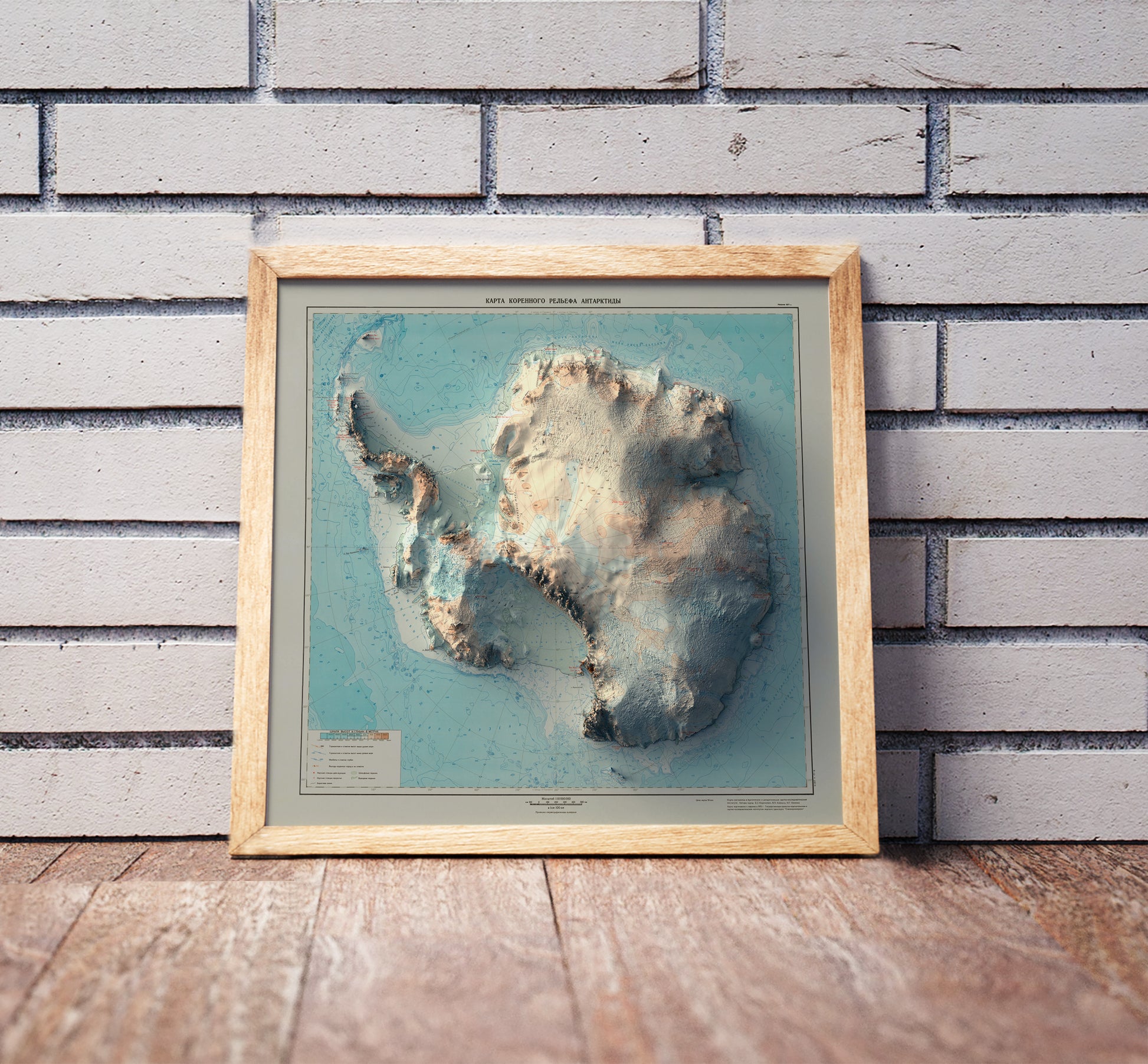Vintage Antarctica shaded relief map in a wooden frame. Realistic terrain art print for home decor, displayed against a brick wall