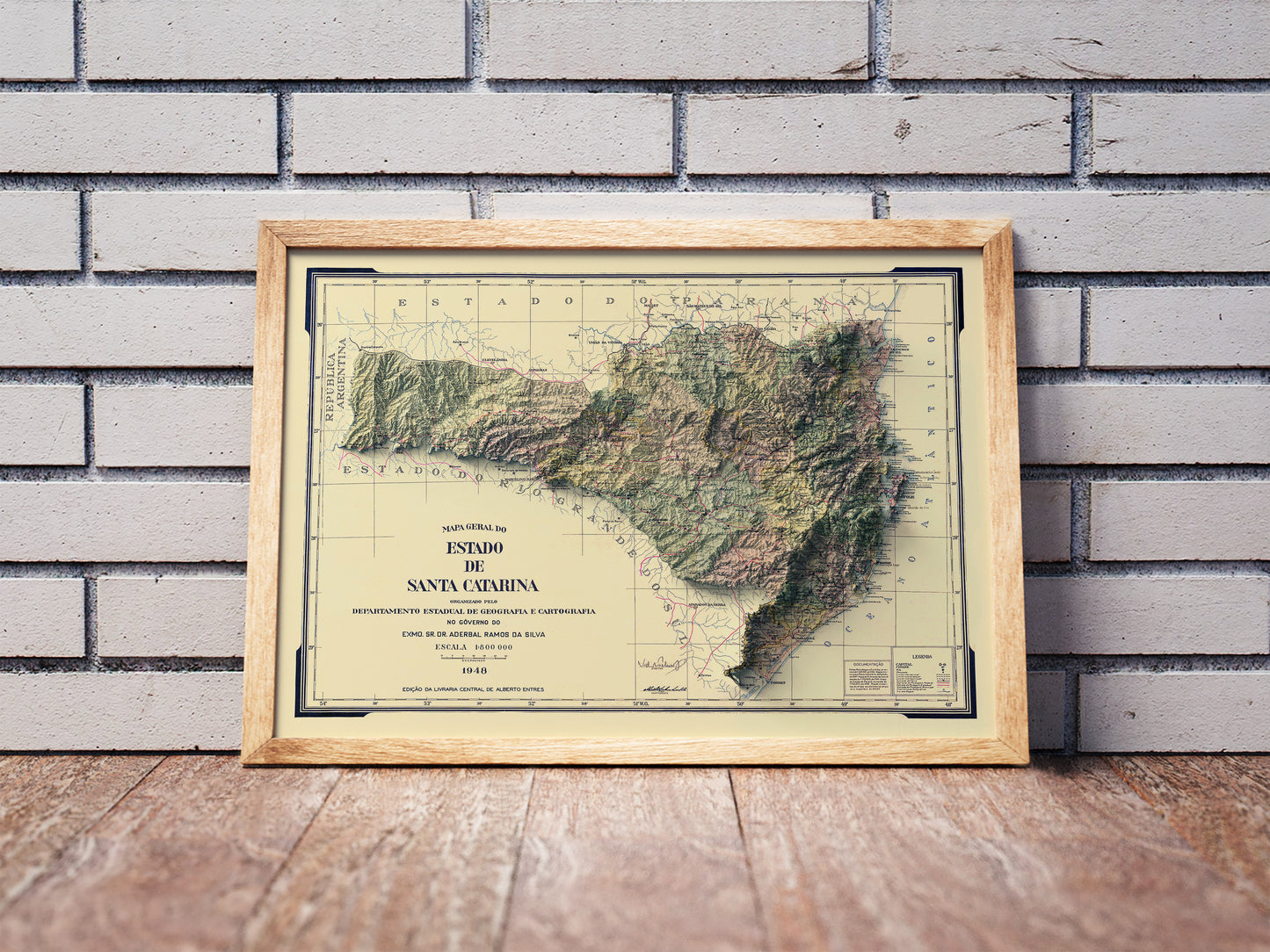 Vintage Santa Catarina shaded relief map in a wooden frame. Realistic terrain art print for home decor, displayed against a brick wall