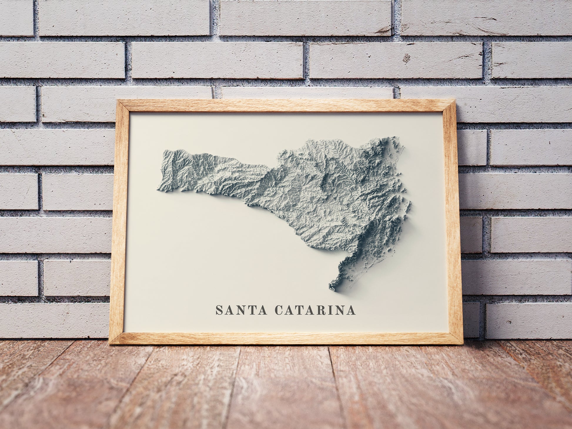 Santa Catarina shaded relief map in a wooden frame. Realistic terrain art print for home decor, displayed against a brick wall