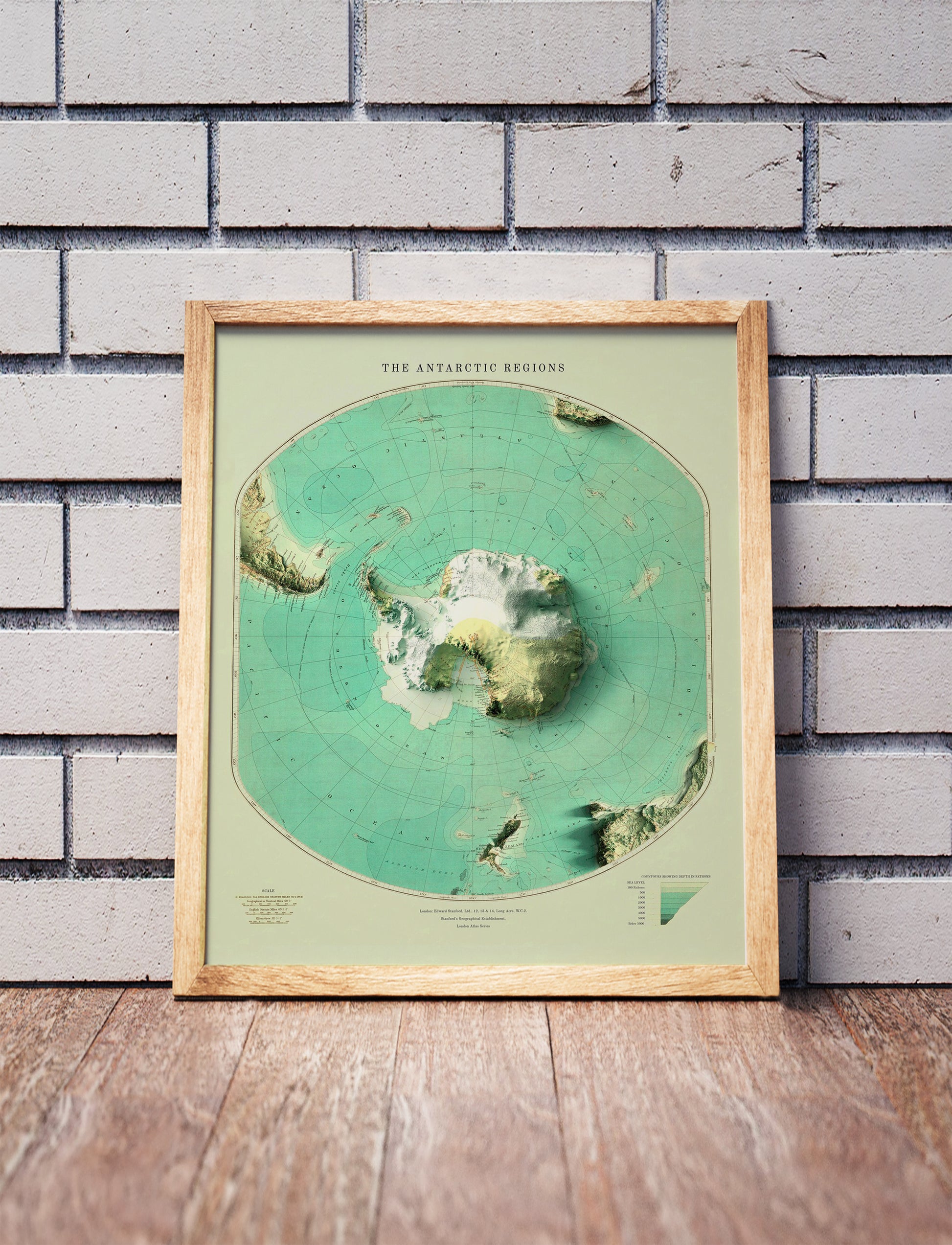 Vintage Antarctica shaded relief map in a wooden frame. Realistic terrain art print for home decor, displayed against a brick wall