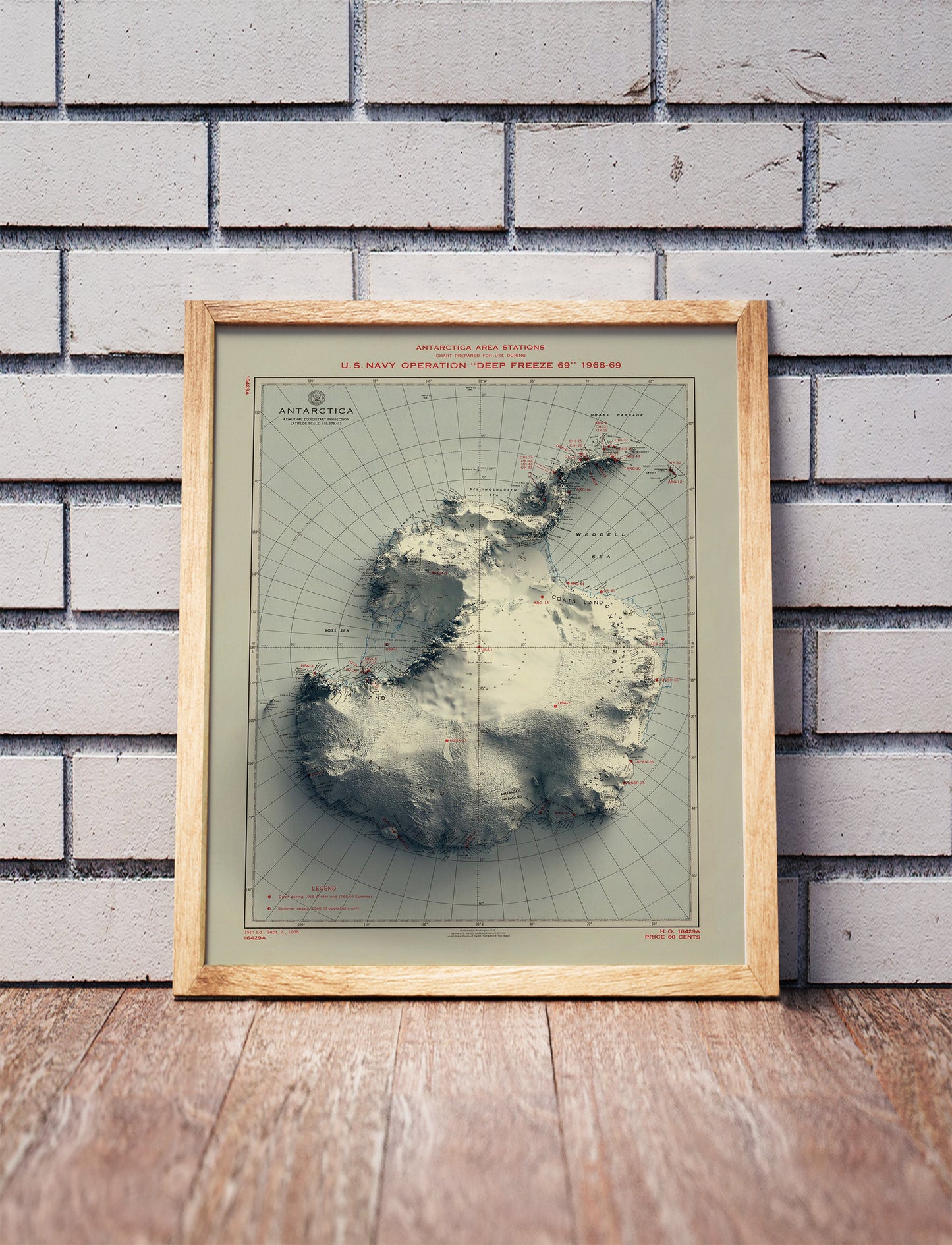 Vintage Antarctica shaded relief map in a wooden frame. Realistic terrain art print for home decor, displayed against a brick wall