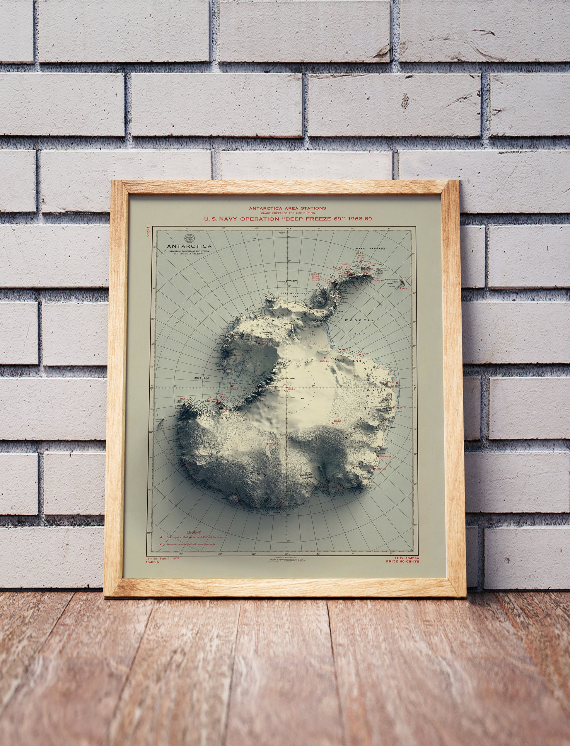 Vintage Antarctica shaded relief map in a wooden frame. Realistic terrain art print for home decor, displayed against a brick wall