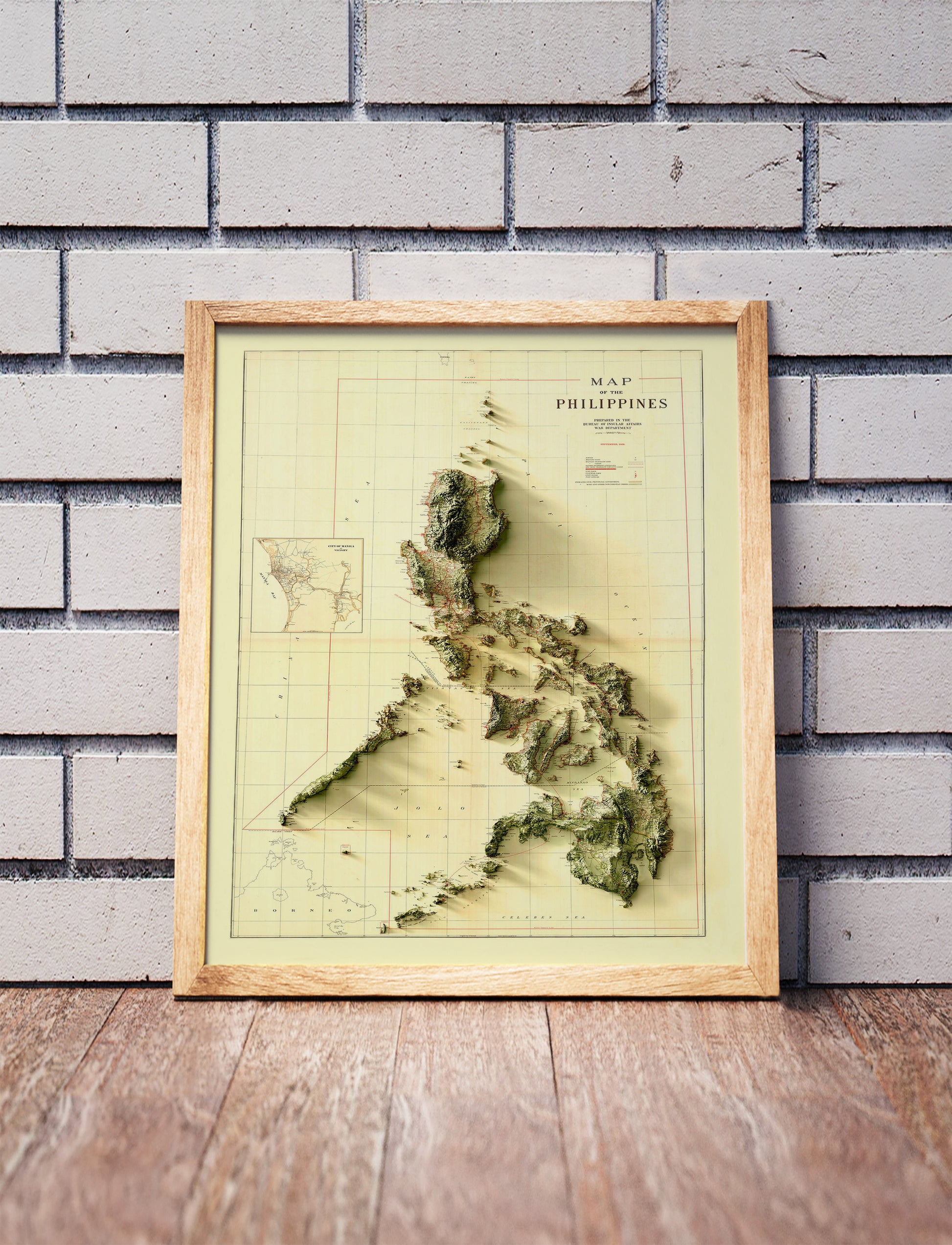 Vintage Philippines shaded relief map in a wooden frame. Realistic terrain art print for home decor, displayed against a brick wall
