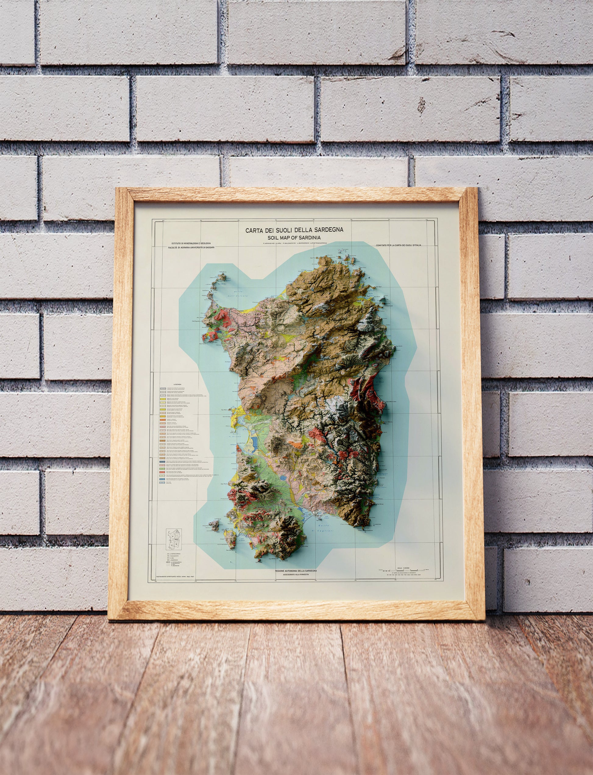 Vintage Sardinia, Italy, shaded relief map in a wooden frame. Realistic terrain art print for home decor, displayed against a brick wall