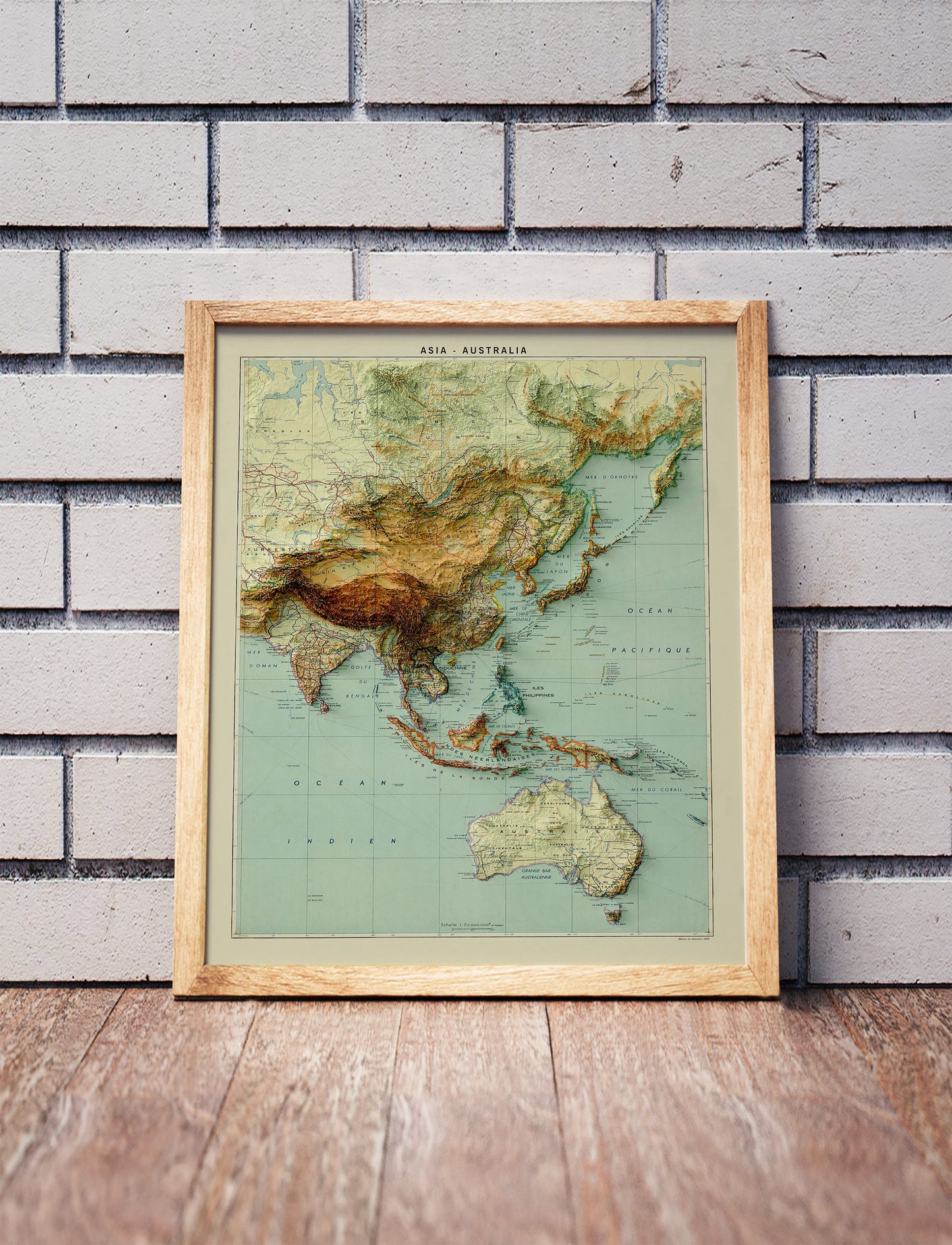 Vintage Asia and Australia shaded relief map in a wooden frame. Realistic terrain art print for home decor, displayed against a brick wall