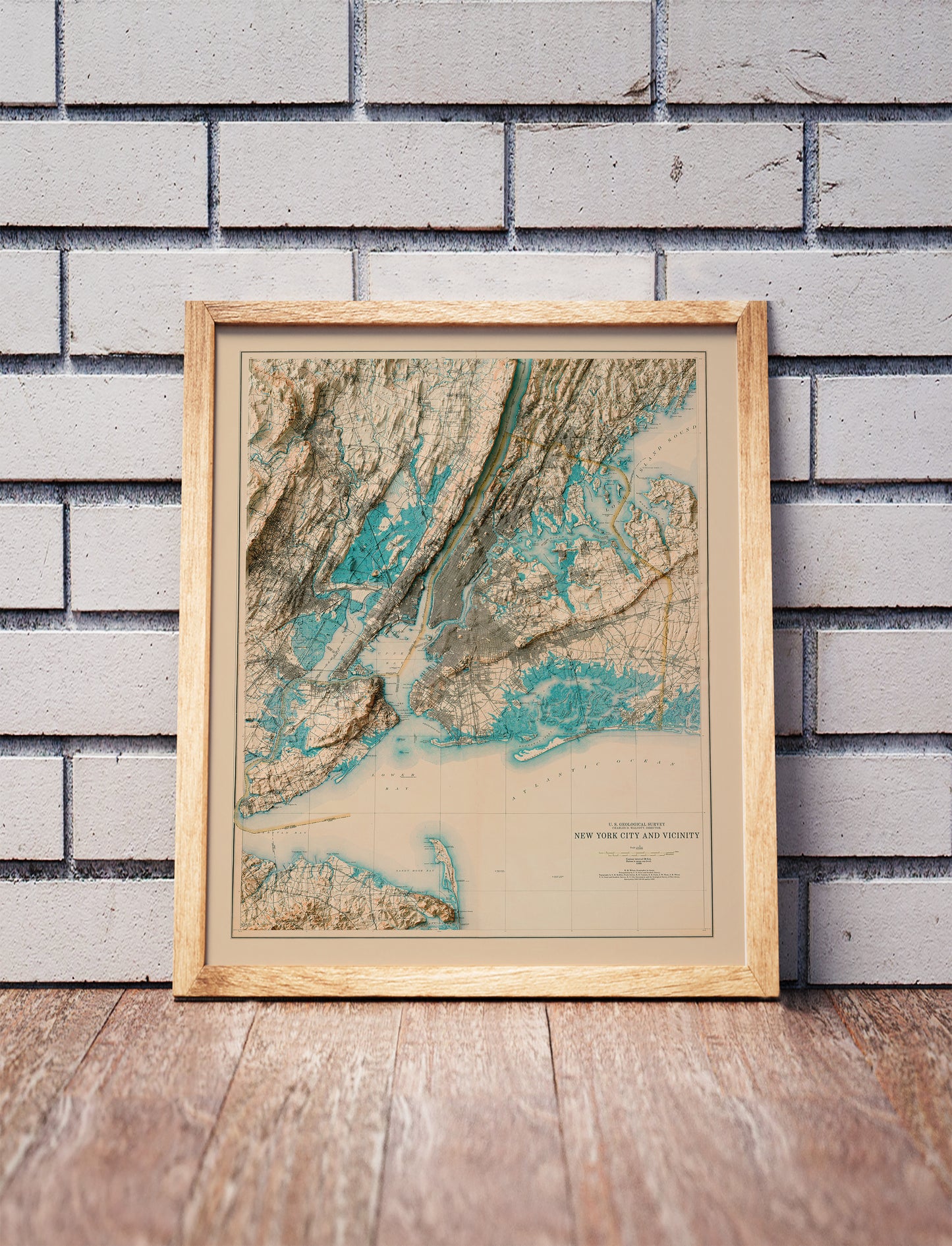 Vintage New York City shaded relief map in a wooden frame. Realistic terrain art print for home decor, displayed against a brick wall