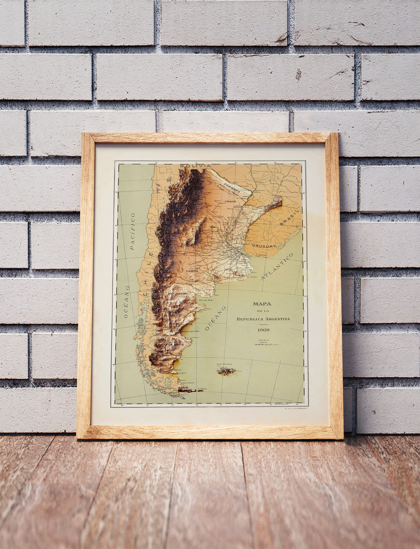 Vintage Argentina shaded relief map in a wooden frame. Realistic terrain art print for home decor, displayed against a brick wall